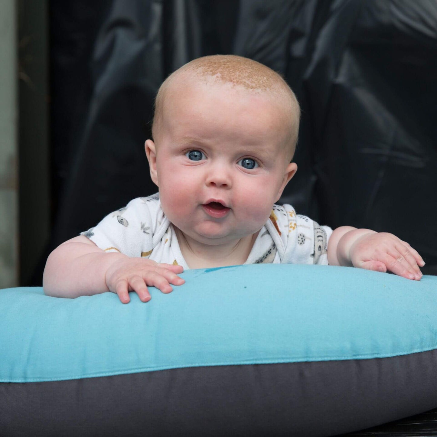 Baby during tummy time resting on a supportive feeding pillow in reef blue and charcoal.