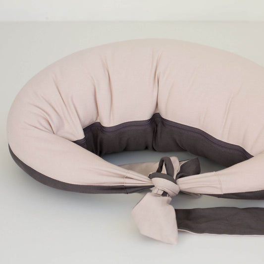 Feeding pillow in dusky pink laid flat with charcoal grey inner panel and long ties stretched out, showing its curved ergonomic design.