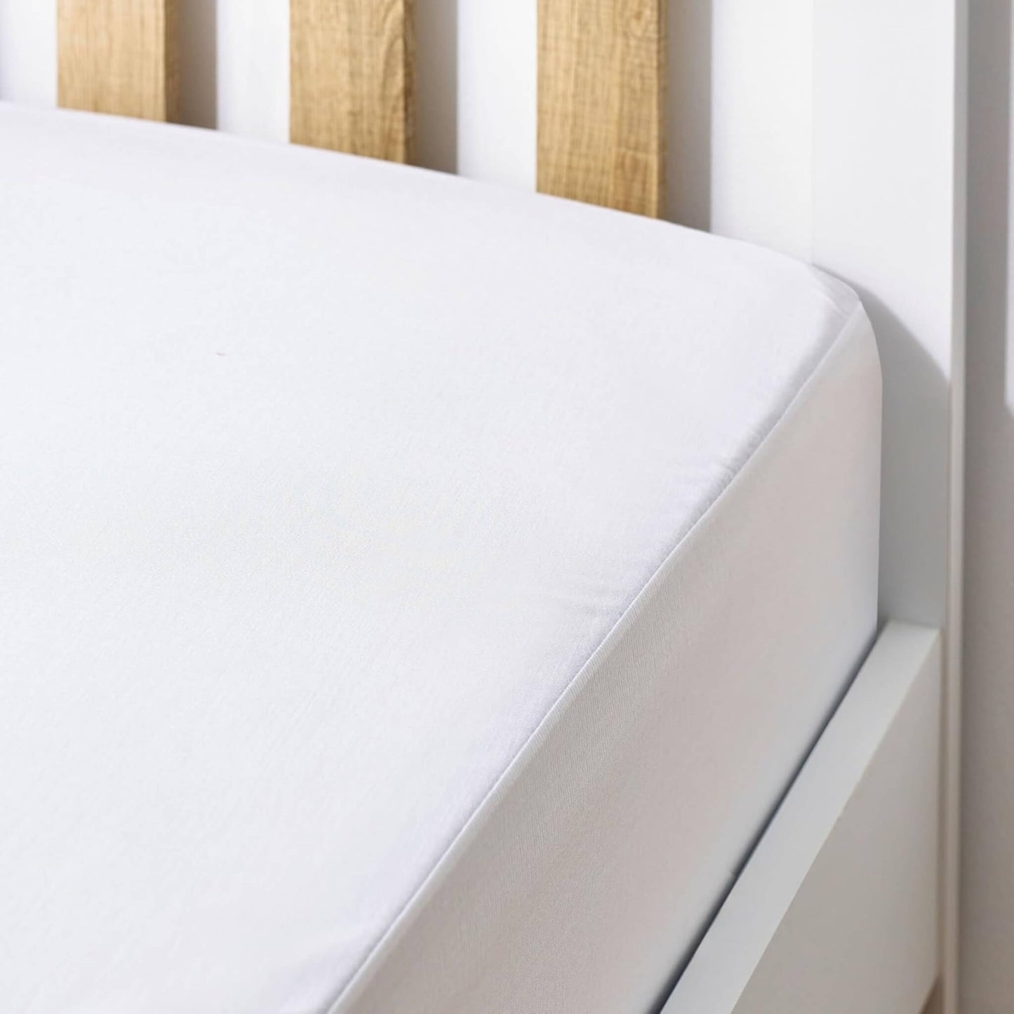 Hippychick Fitted Cotton Mattress Protector shown securely covering a cot mattress with a smooth white cotton finish.