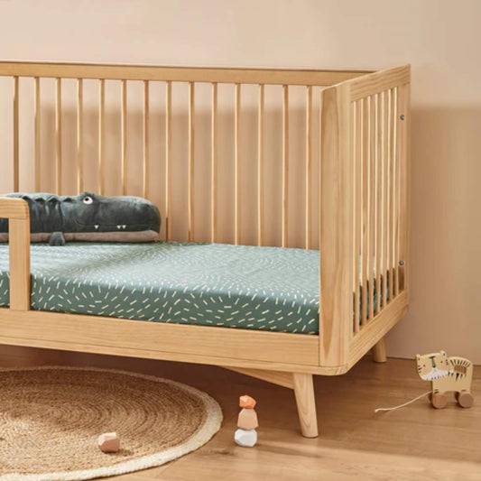 Organic cotton fitted sheet in Dashes print shown on a wooden cot bed with sage green mattress cover and neutral nursery setting.