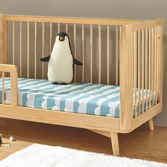 Cot bed styled with a light wood frame and a blue rolling cloud fitted sheet, showing scale and pattern in a nursery setting.