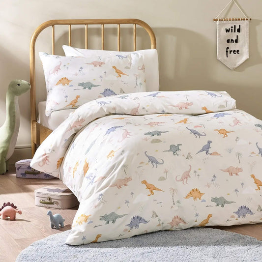 A child’s bed dressed with a cream duvet cover and pillowcase featuring hand-drawn dinosaurs in soft pastel colours, photographed in a calm bedroom setting.