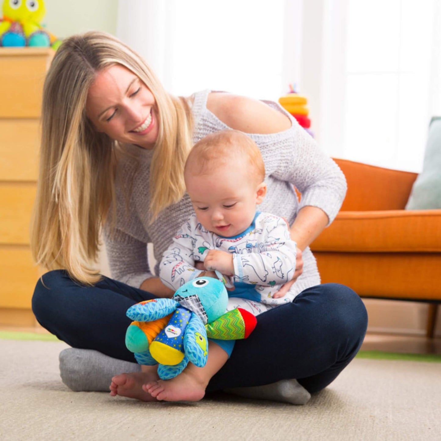 Baby sitting on mother's lap exploring a soft octopus toy with bright colours and textured fabrics to stimulate touch and curiosity.