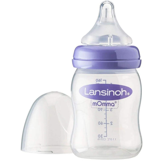 Close-up of baby feeding bottle with clear measurement markings, purple collar and transparent silicone teat, lid resting beside the bottle.