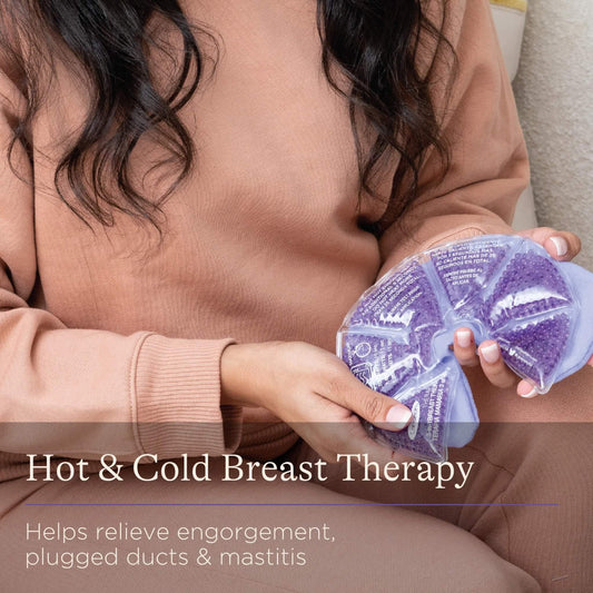 A woman in a beige sweatshirt holding a purple reusable breast therapy pack with a soft fabric cover against her lap.
