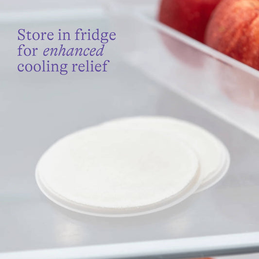 Reusable nipple cooling pads stored in a fridge drawer beside apples, showing how chilling enhances the soothing relief for sore or cracked nipples.