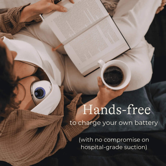A woman relaxing with an open book and holding a mug while wearing a hands-free breast pump inside a white nursing bra.