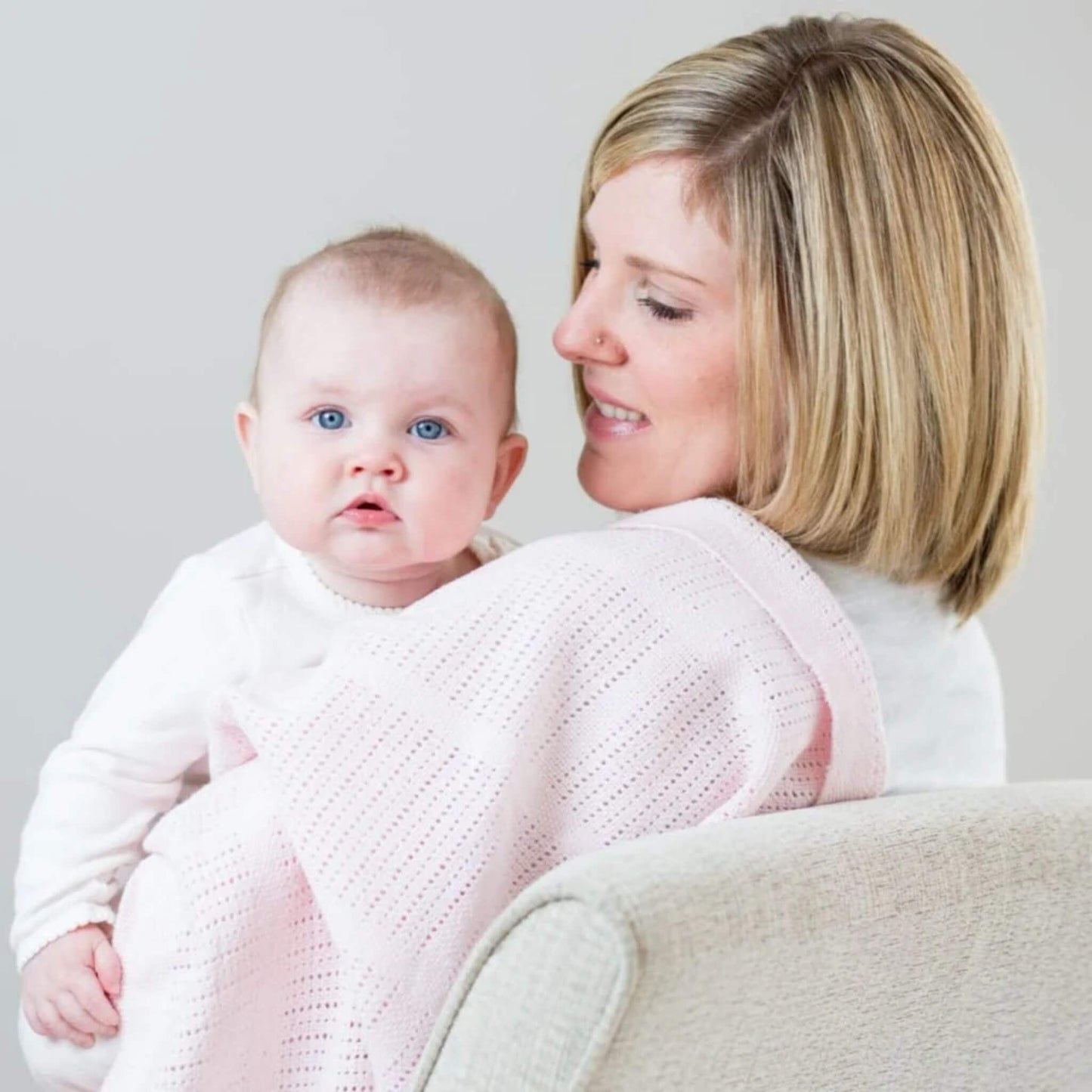 Mother holding baby wrapped in soft pink Lulujo cellular blanket, demonstrating the lightweight comfort and breathable weave pattern perfect for bonding and temperature regulation.