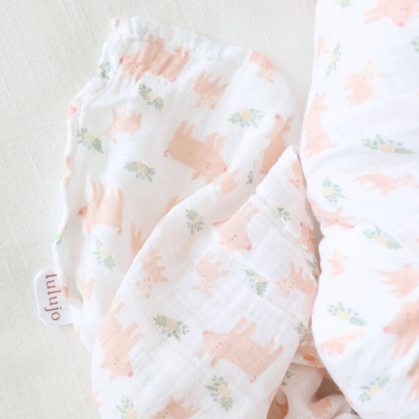 Close-up of the cotton muslin fabric showing the fine weave and repeating pig and floral design in soft pastel tones.