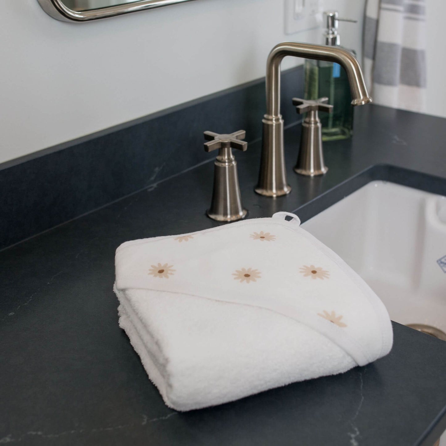 Folded Lulujo daisy hooded towel on dark marble bathroom counter beside brushed nickel faucet and white sink.
