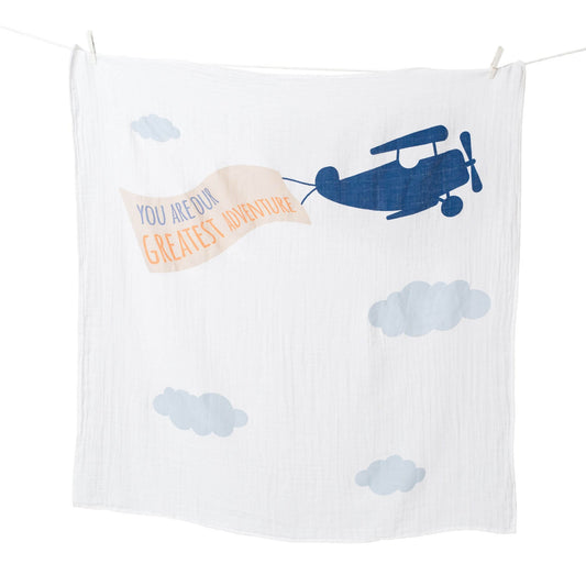 Lulujo white muslin blanket with blue airplane design and banner reading 'You Are Our Greatest Adventure' hanging on clothesline.