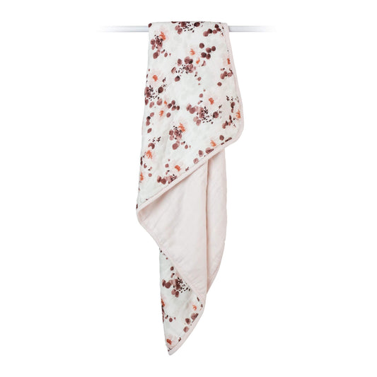 Lulujo quilted blanket displayed hanging, showcasing the delicate eucalyptus print pattern and soft drape. The reversible design features white backing with elegant edge binding.