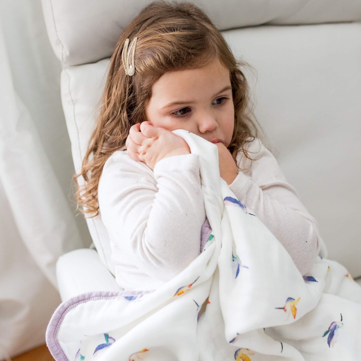 Child cuddling with Lulujo hummingbird print blanket, showing its comfort and softness.