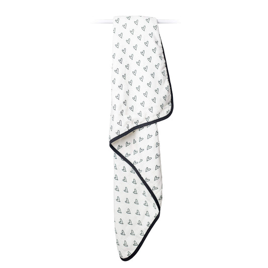 Lulujo Quilted Blanket in Messy Heart print draped over a rail, showing its lightweight, breathable muslin fabric.