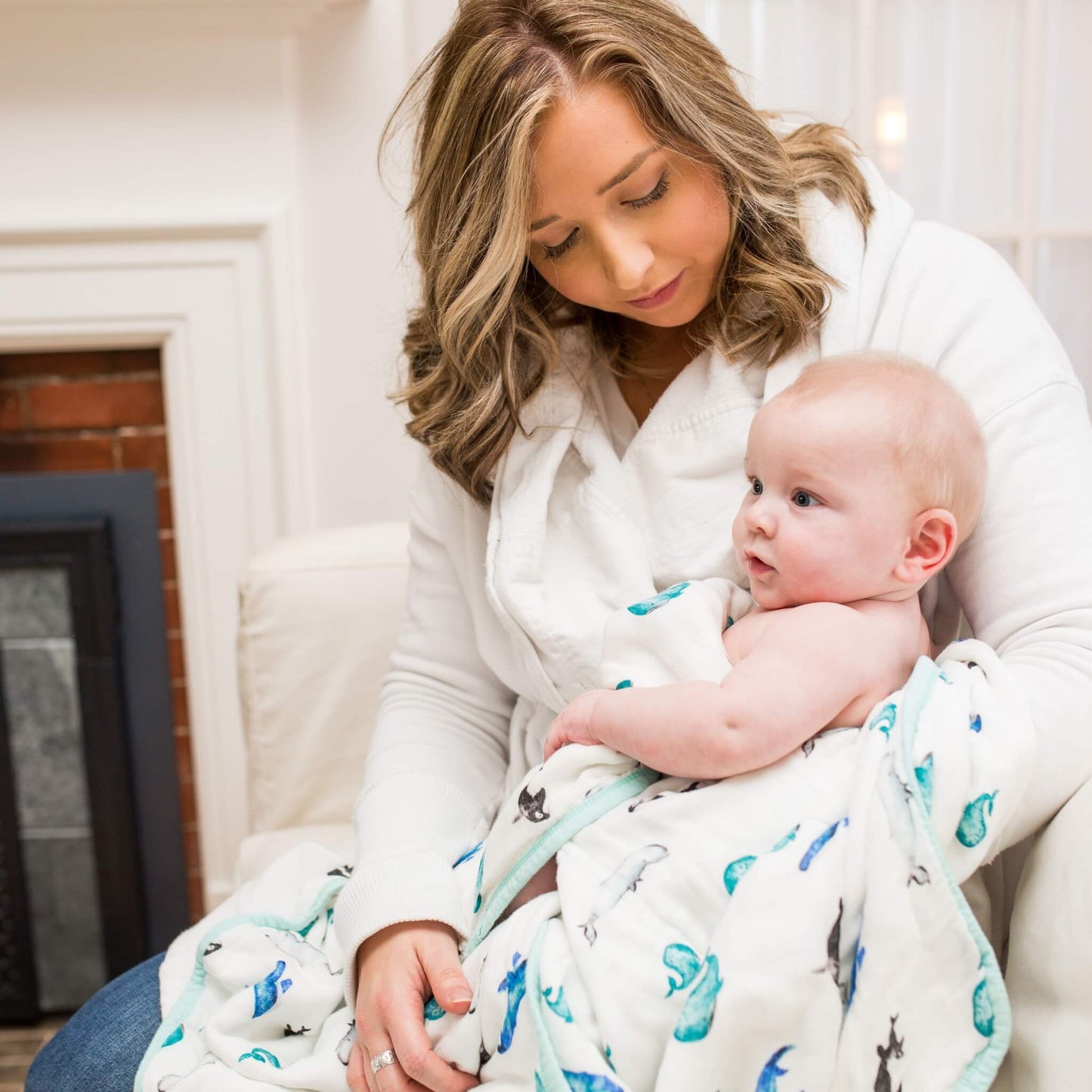 A mother gently cradles her baby in the Lulujo Quilted Blanket in Whale print, creating a cosy and soothing moment.
