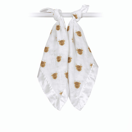 Two soft muslin comfort blankets tied onto a rail, featuring a repeating brown highland cow pattern with silky satin edging.