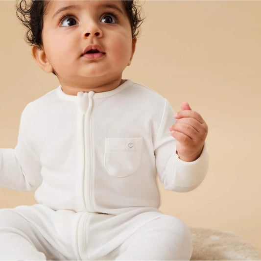 A baby wearing a white sleepsuit, shown in a seated pose with the long front zip and small chest pocket visible.