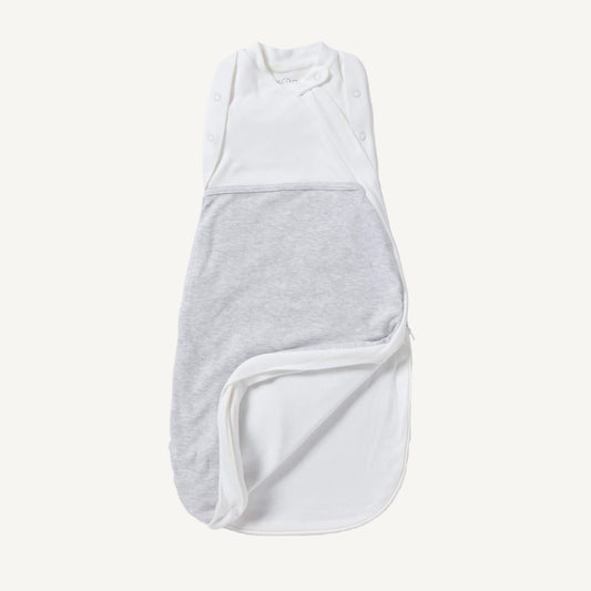 A newborn swaddle bag in grey shown partially unzipped at the bottom, revealing the soft inner lining and wrap-style chest panel with poppers.