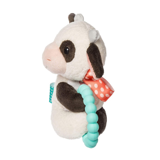 A side view of a plush cow baby rattle holding an aqua teething ring with a red polka dot ribbon tied at the neck.