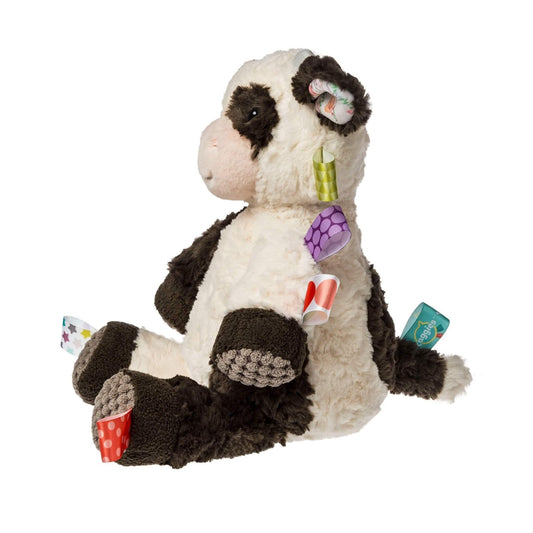 Side view of a soft cow cuddly toy in cream and black with textured foot pads, floppy ears and satin ribbon tags around its body and tail.