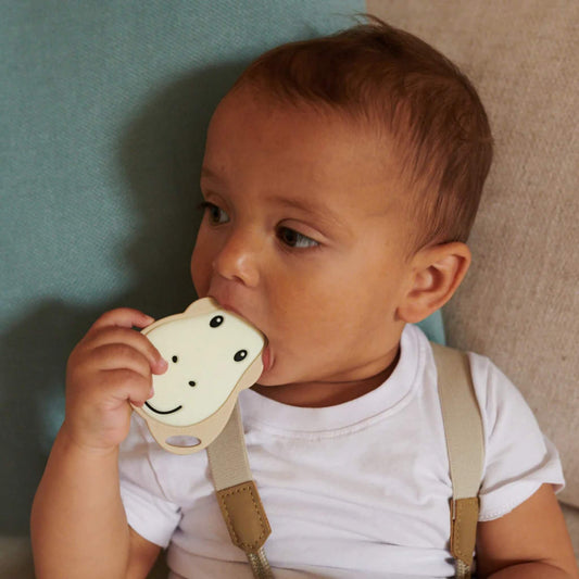 Baby holding a flat giraffe-shaped teether and chewing on the soft silicone surface.