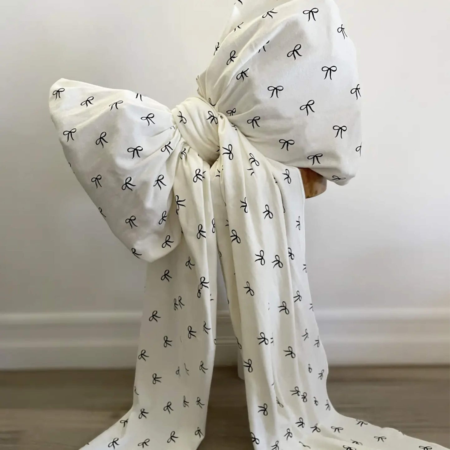 Large tied bow created from light fabric with a repeating small-bow print, displayed against a plain wall.