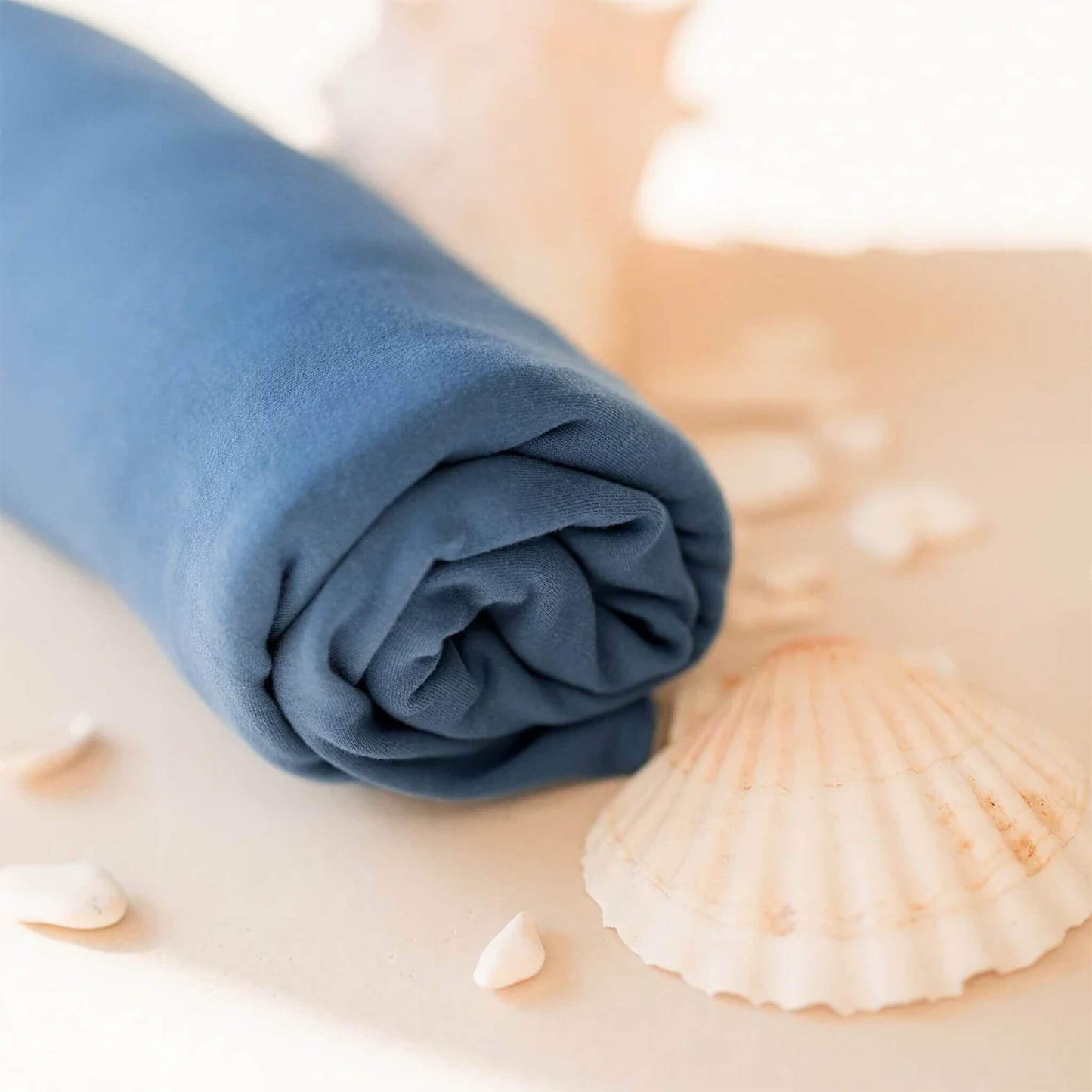 Rolled Ocean blue baby wrap placed beside seashells on a neutral background.