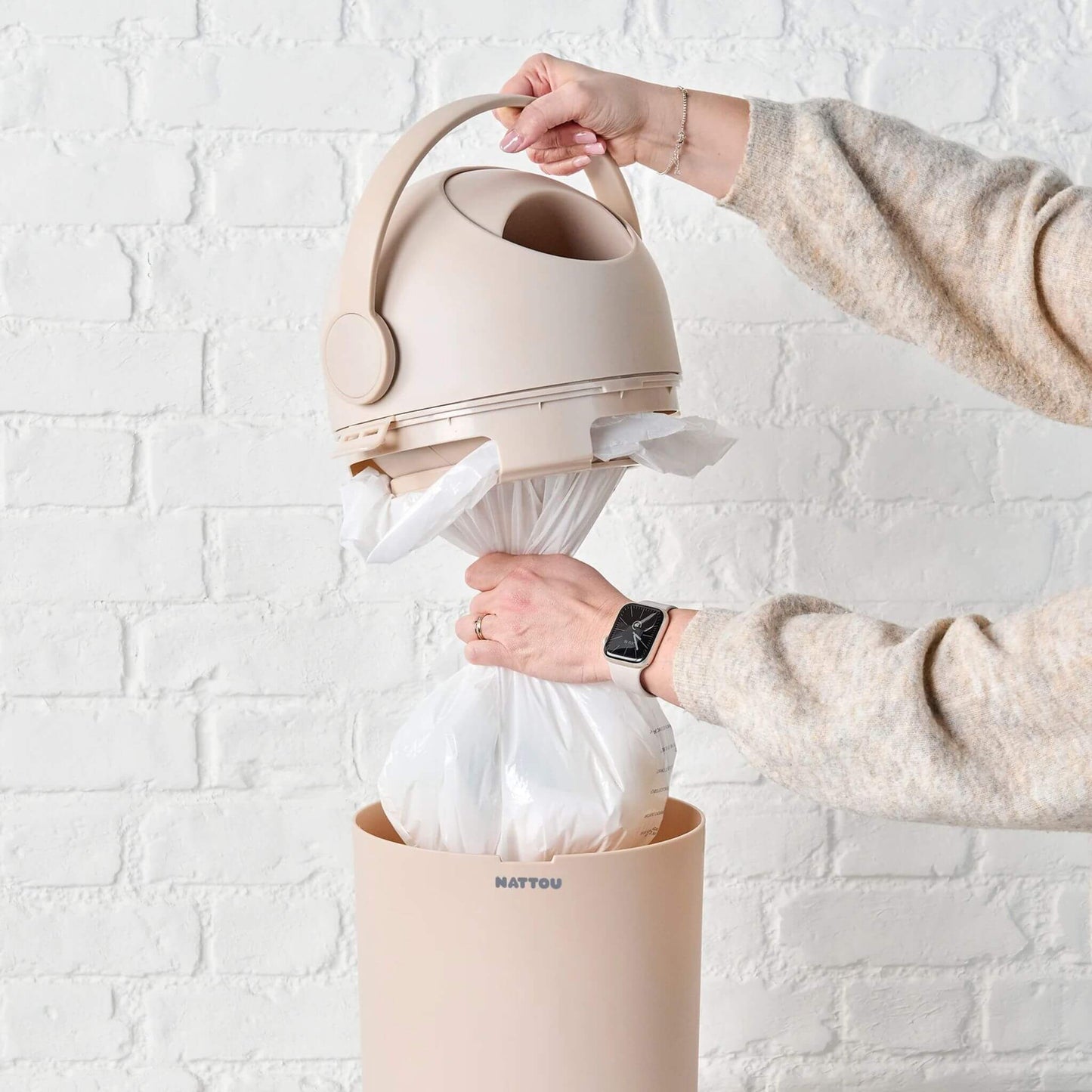 A person removing a full plastic bag from a beige nappy bin highlighting its compatibility with standard bin liners.