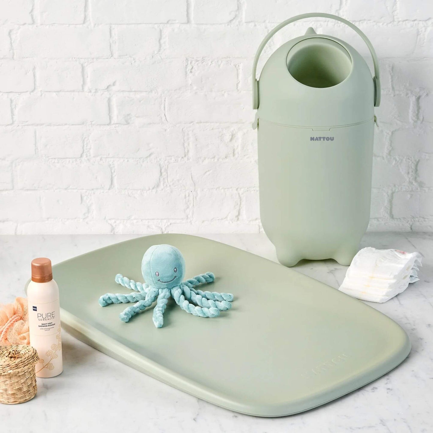 A green nappy bin in a nursery setup, placed next to a matching changing mat and baby essentials.