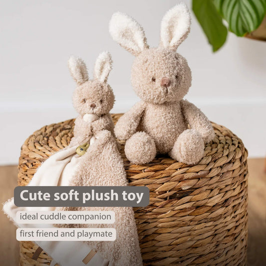 A small plush bunny and a matching comforter displayed on a woven basket, both made with soft textured fabric in light beige.