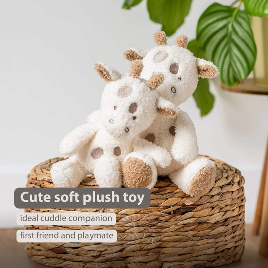 Two soft giraffe plush toys resting together on a woven basket, with on-image text reading “Cute soft plush toy”, “ideal cuddle companion” and “first friend and playmate.” Plush bodies appear cream with brown spots and textured horns, set against a neutral backdrop.