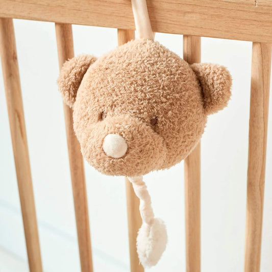 Soft Musical Teddy Bear attached to wooden crib, with beige plush face and white pull cord for gentle bedtime melodies