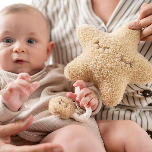 Baby holding the plush star shaped musical cuddly while seated, gently pulling the music cord.