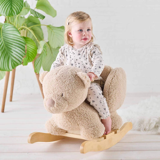 Smiling toddler riding the soft fabric Teddy Bear Rocker in a cosy, light-filled room with natural wooden accents.