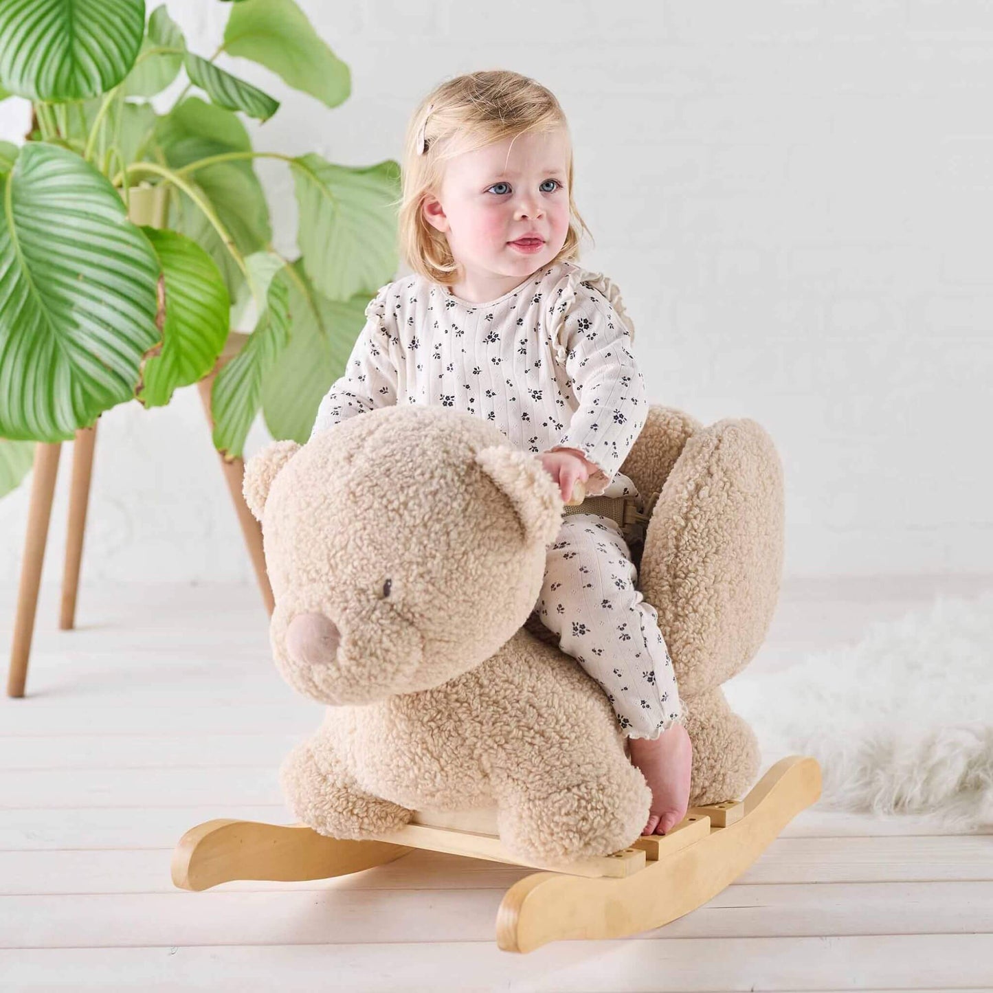 Smiling toddler riding the soft fabric Teddy Bear Rocker in a cosy, light-filled room with natural wooden accents.