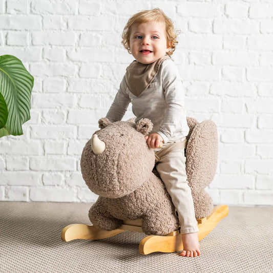 Smiling toddler sits on a plush rhino rocker with a sturdy wooden base, enjoying a safe and cosy rocking experience.