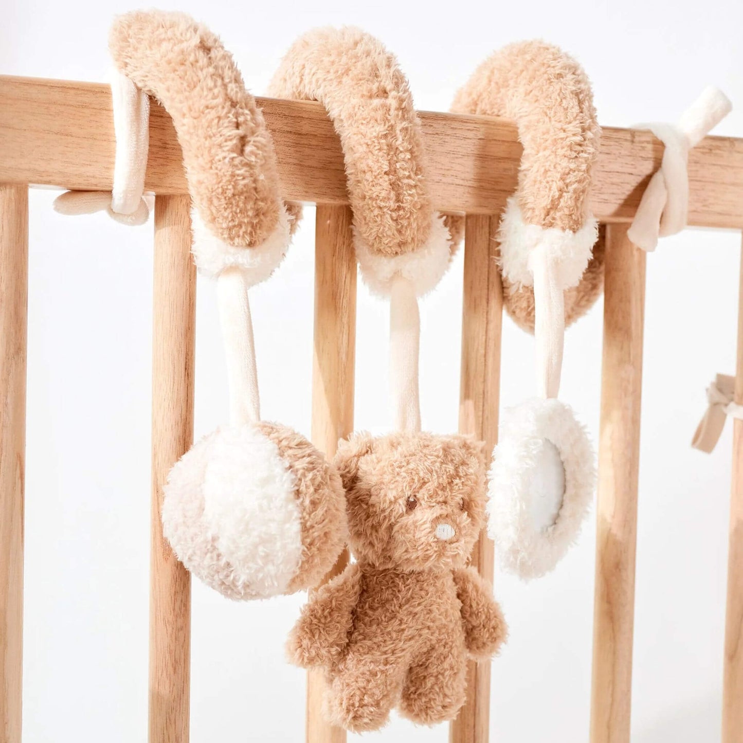 Activity spiral crib toy featuring a soft plush teddy bear and textured balls, mounted on wooden nursery furniture.