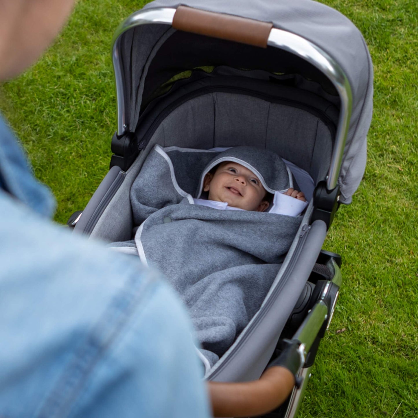 Baby lying in a pushchair with grey hooded blanket fabric arranged around the head and body.