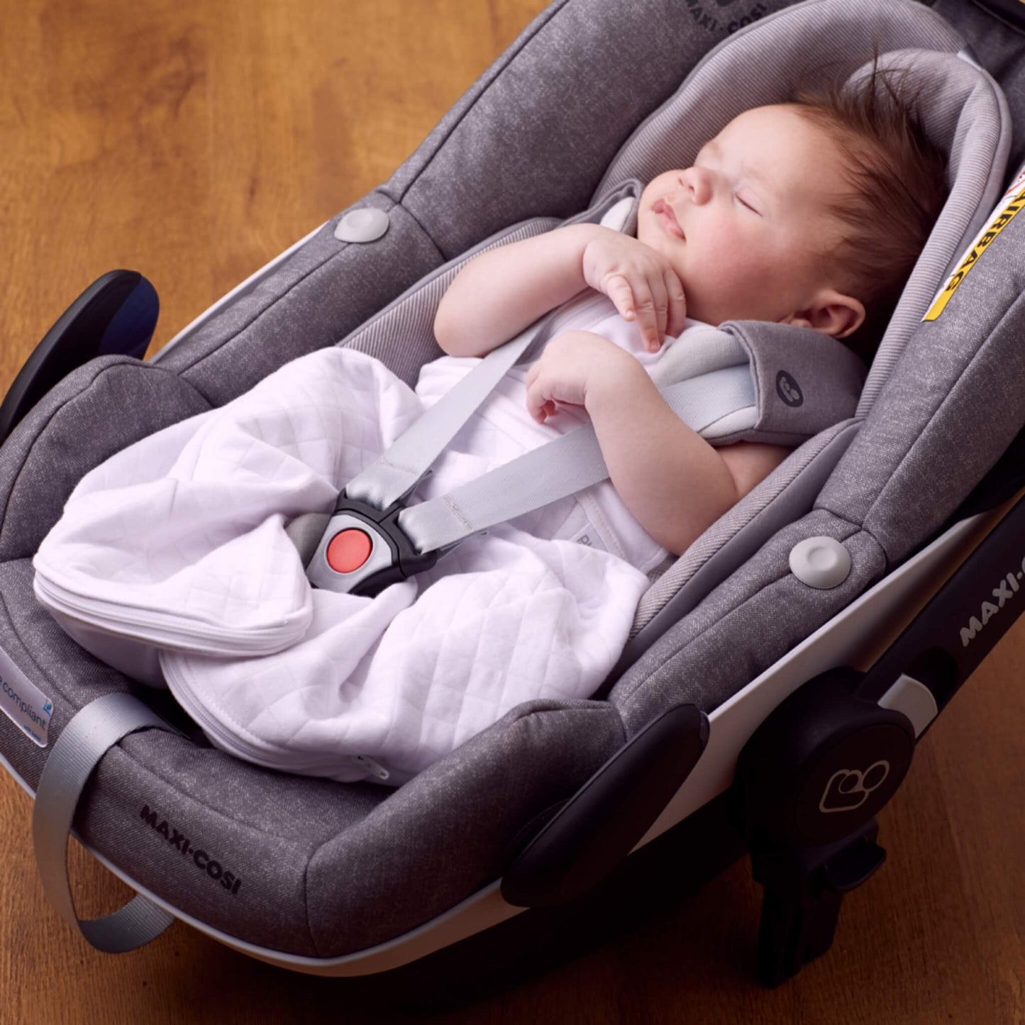 A baby sleeping in a car seat while wearing a lightweight swaddle sleep bag, showing compatibility with travel harnesses.