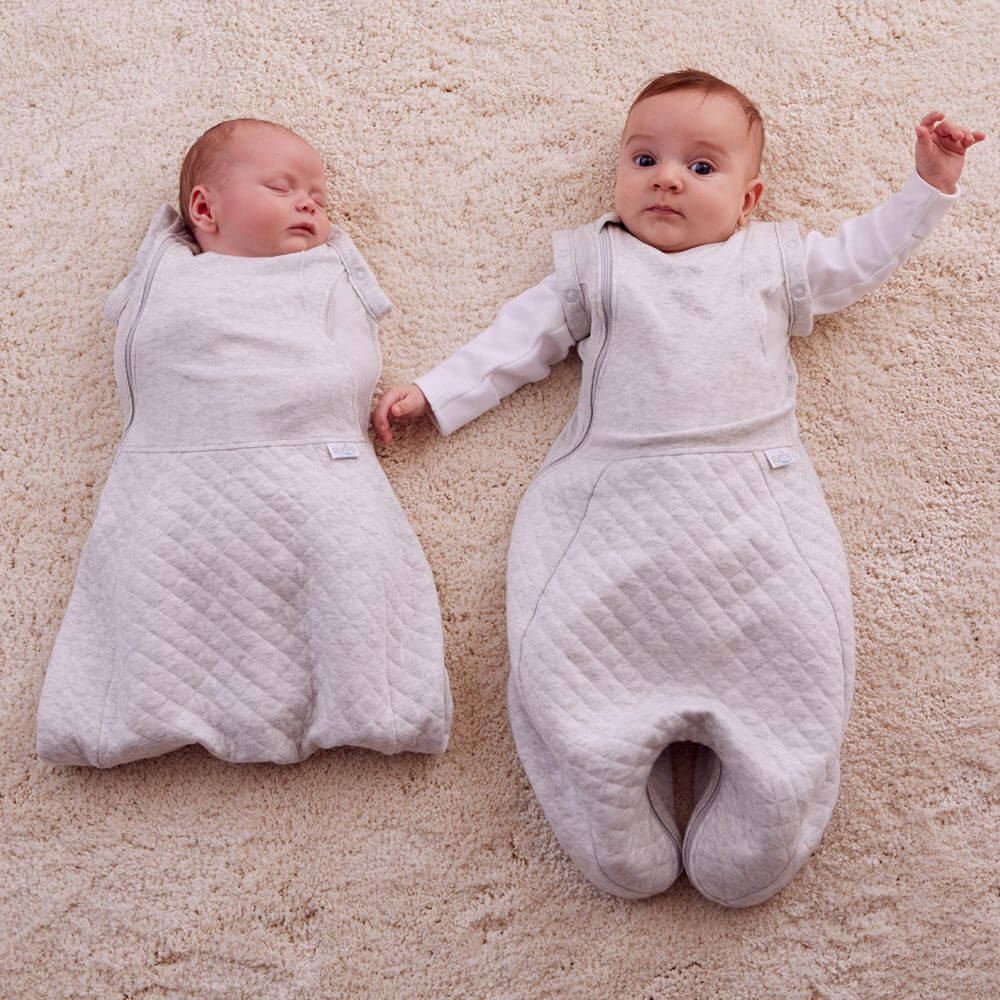 Two babies side by side in different sizes of the Purflo Swaddle to Sleep Bag 0.5 Tog. Adjustable fit and breathable for safe sleep.