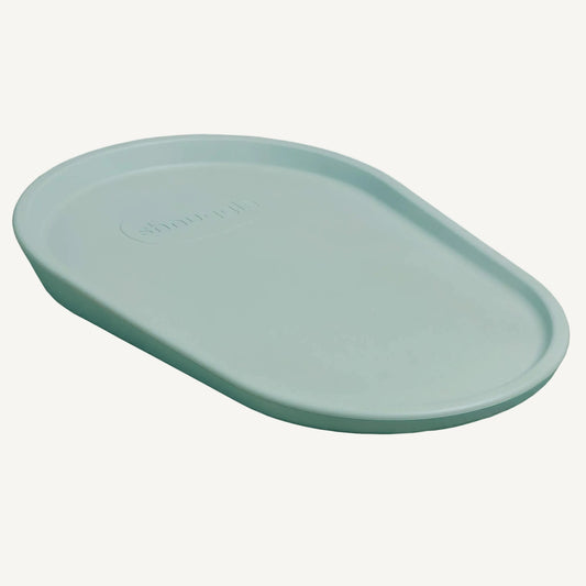 A eucalyptus green baby changing mat shown from an angled view, highlighting the smooth wipe-clean surface and softly raised edges.