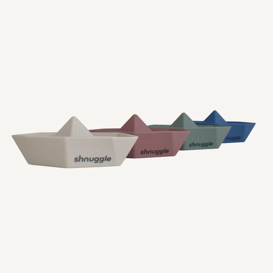 A row of four bath boats in muted neutral colours, each shaped with a raised sail and flat base.