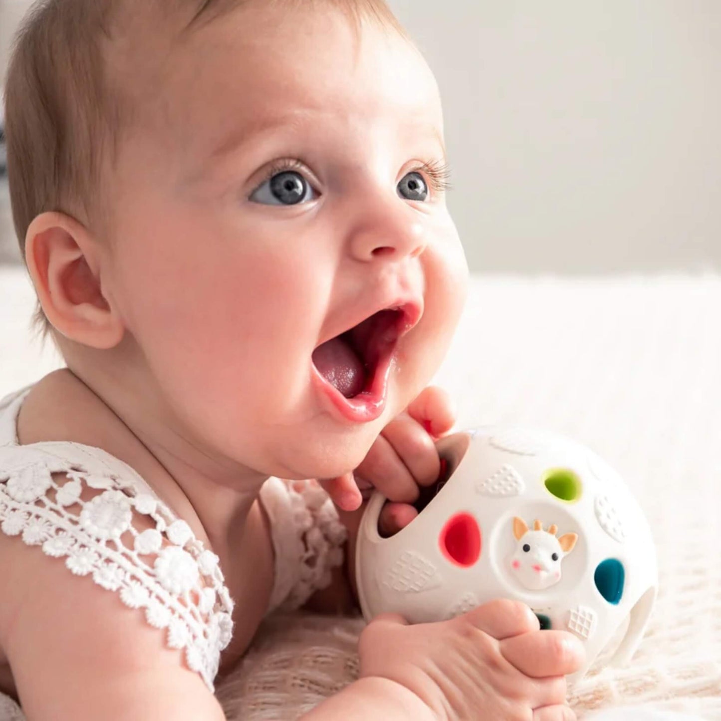 Baby holding and exploring a textured sensory ball with finger holes, raised surfaces, and colourful rubber details.