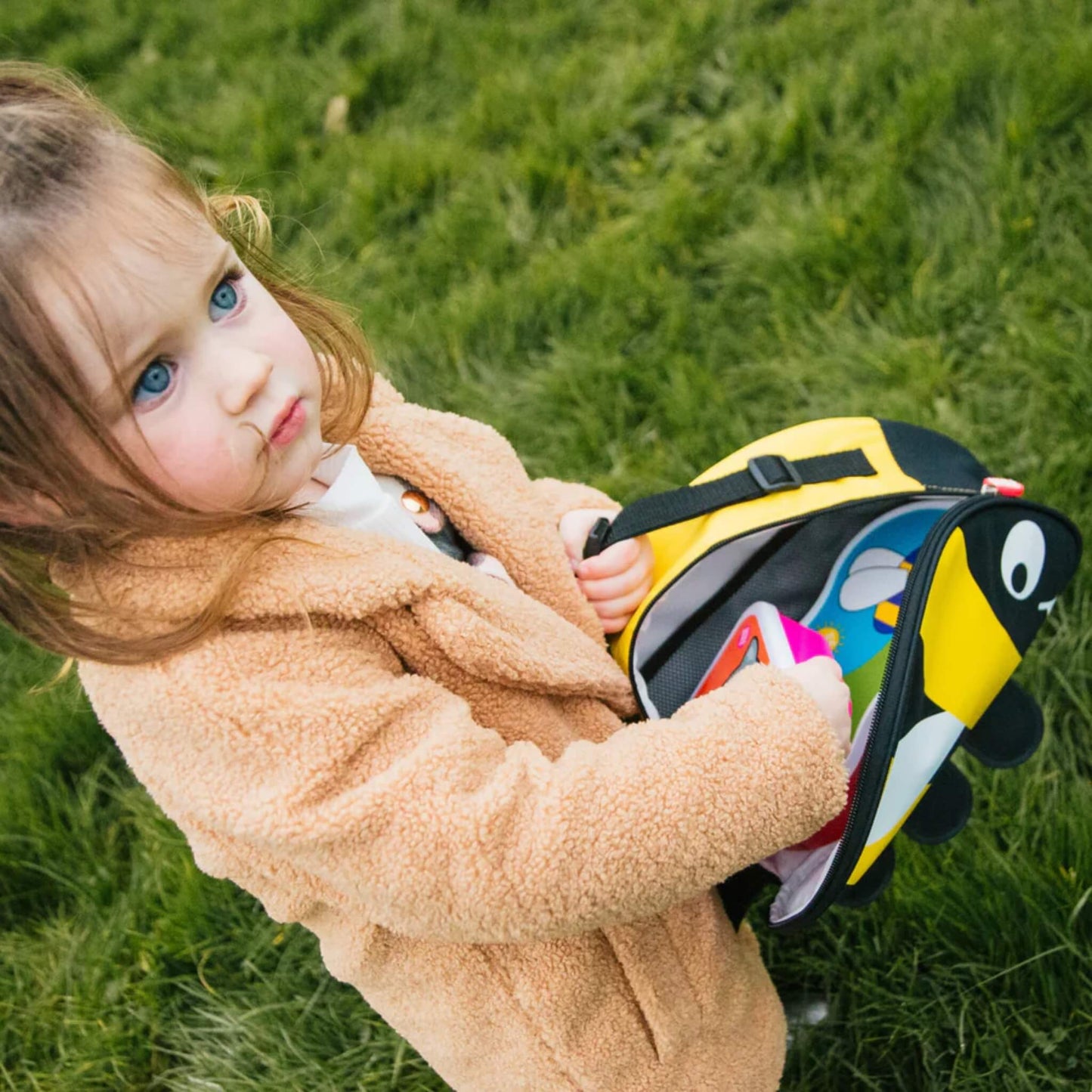 Child holding open bee-shaped insulated lunch bag outdoors, showing lunch items inside and clipped carry handle in use.
