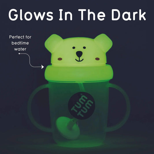 A glow-in-the-dark sippy cup with a bear-shaped lid, shown glowing green in the dark. The image includes text overlays reading 'Glows In The Dark' and 'Perfect for bedtime water' with a dotted arrow pointing to the cup.