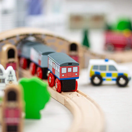 Close-up of the wooden Underground Train approaching the stone-effect bridge, with a toy police car and London buildings in the background.