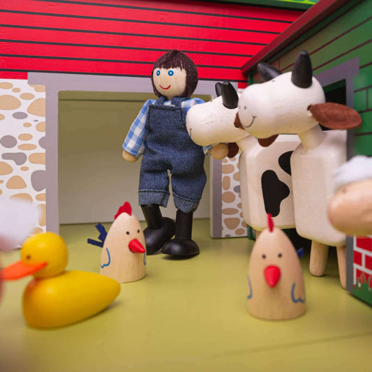 Farmer figure in blue overalls stands among farm animals near a wooden barn and red stable building.