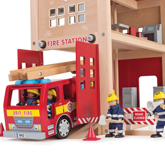 Wooden fire engine driving out from the fire station as firefighter figures prepare with cones and road signs.