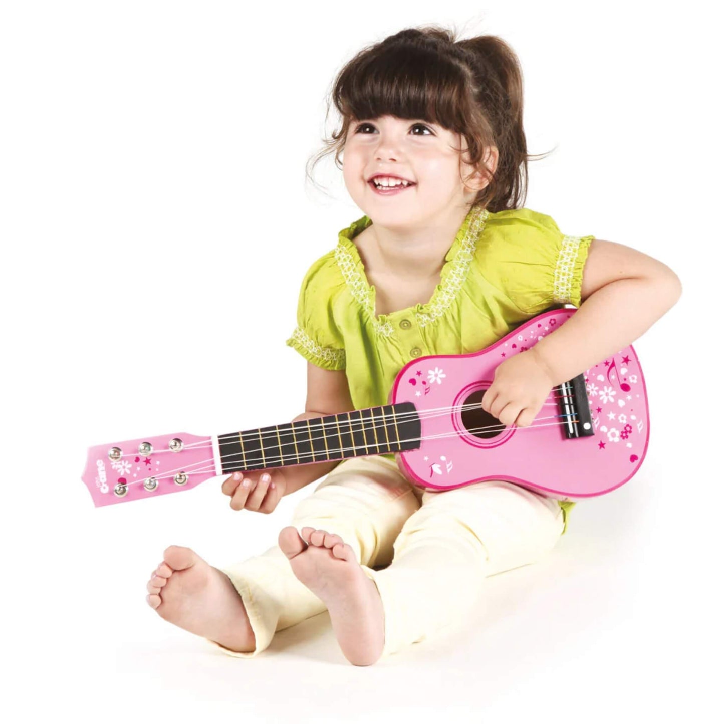 Smiling toddler sitting cross-legged and playing the guitar, with the instrument resting comfortably across their lap.