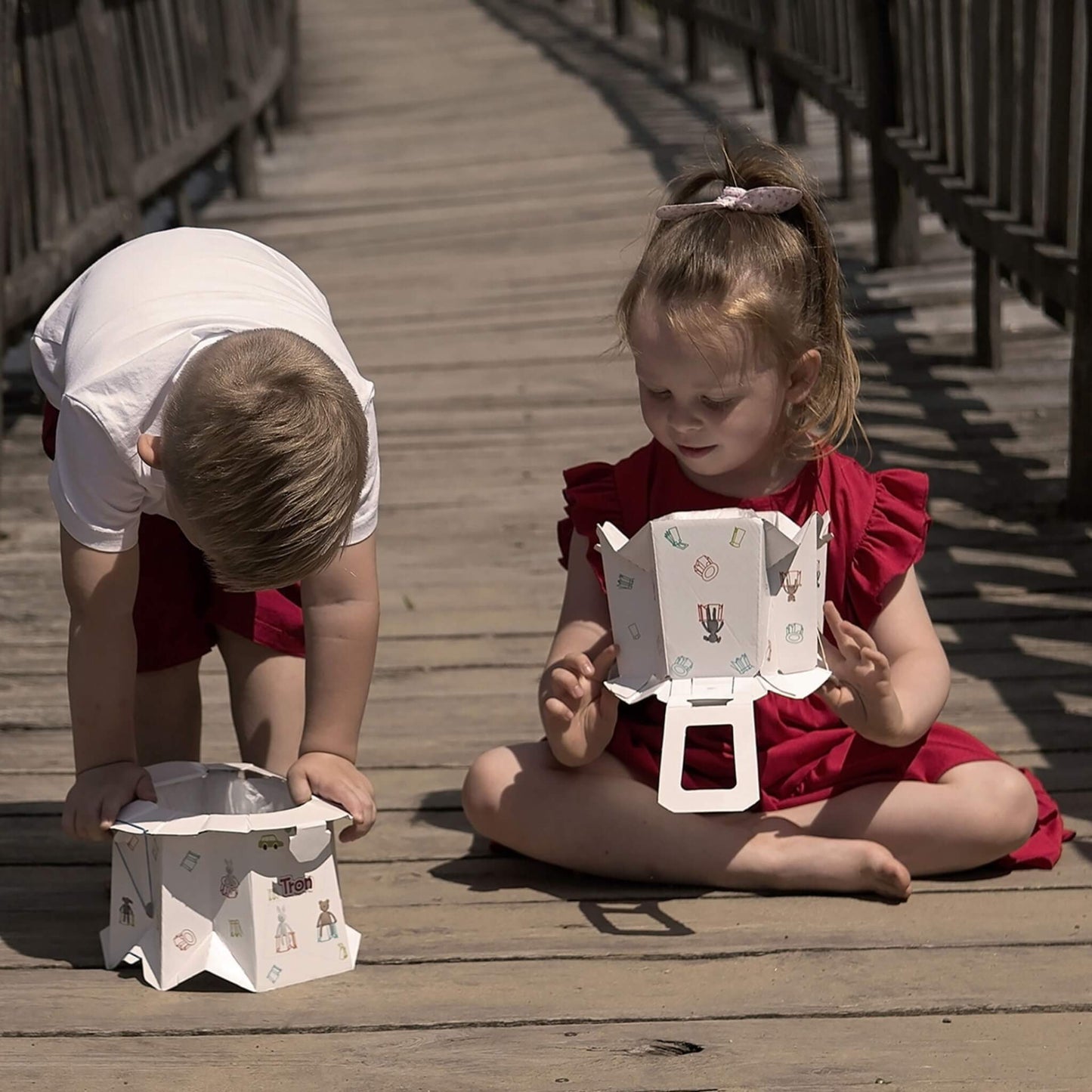 Two children playing with disposable potties outdoors on a wooden path, exploring the foldable design.